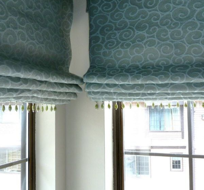 Blue decorative window shades are partially rolled up on the corner windows of an apartment.