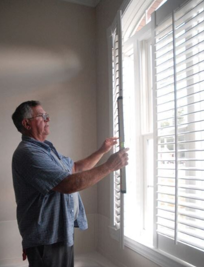 Window shutter contractor repairs the hardware on a pair of plantation shutters in the bathroom of a home.