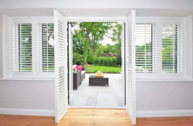 Plantation shutters and an open door facing the back yard with green grass and a patio.